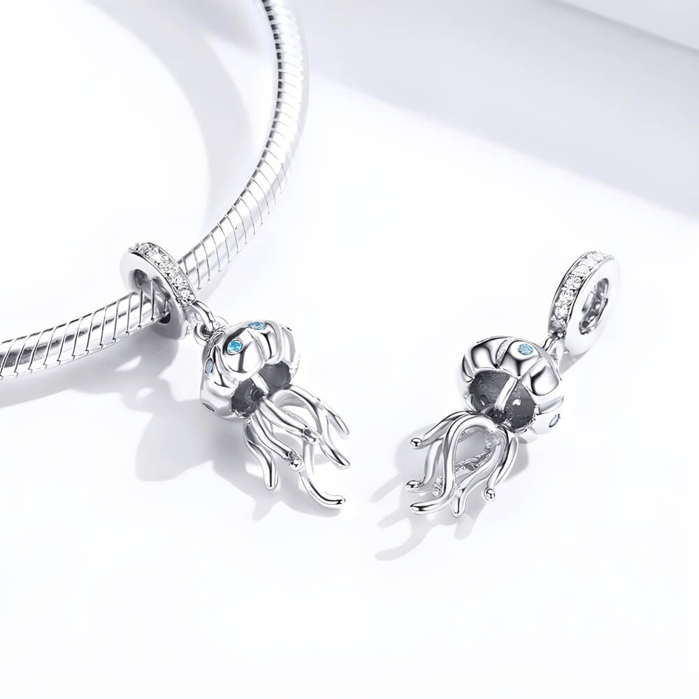 Sterling silver jellyfish charm with blue stones on the bell and long flowing tentacles, hanging from a bail set with clear crystals