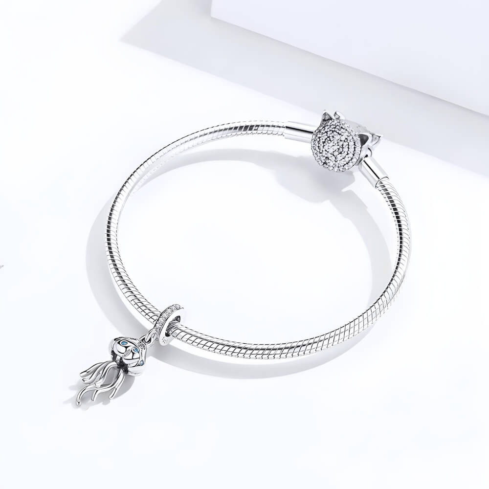 Sterling silver jellyfish charm with blue stones on the bell and long flowing tentacles, hanging from a bail set with clear crystals
