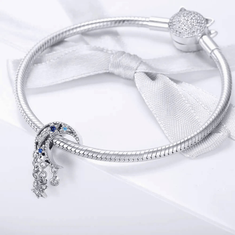Sterling silver crescent moon charm with clear, dark blue, and light blue stones, featuring three dangling star and circle crystal accents