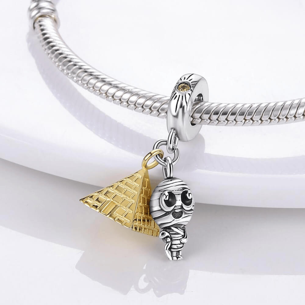 Sterling silver charm with two dangles: a gold pyramid and a small mummy figure with black eyes, plus a bail accented with a yellow stone 