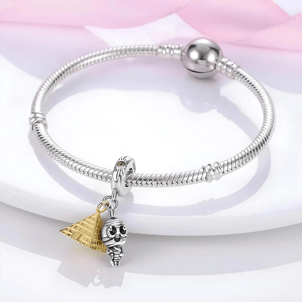 Sterling silver charm with two dangles: a gold pyramid and a small mummy figure with black eyes, plus a bail accented with a yellow stone 