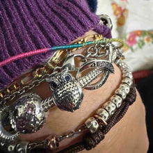 Sterling silver owl charm with textured feather design, blue eyes, and clear gemstones.