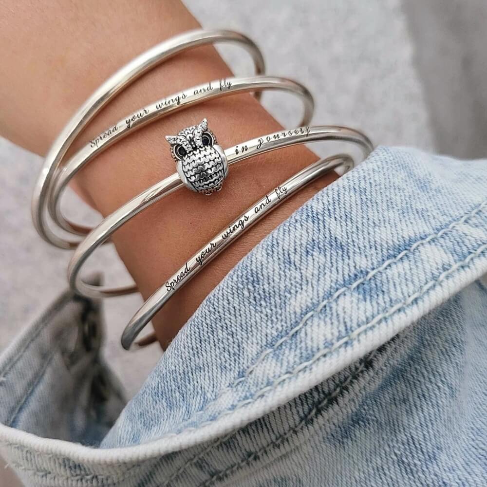 Sterling silver owl charm with textured feather design, blue eyes, and clear gemstones.