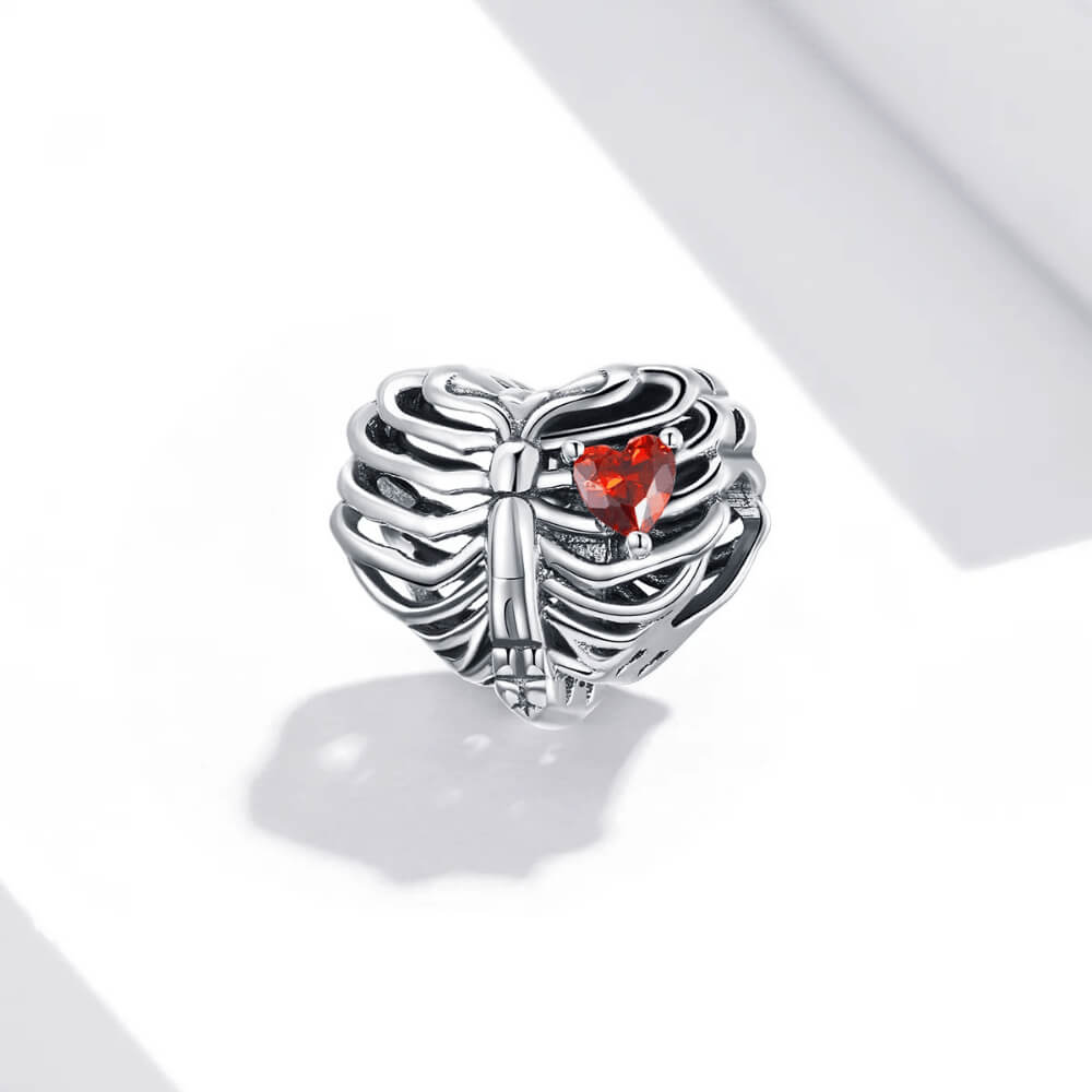 Sterling silver ribcage-shaped charm with an openwork design and a small red heart-shaped crystal inside 