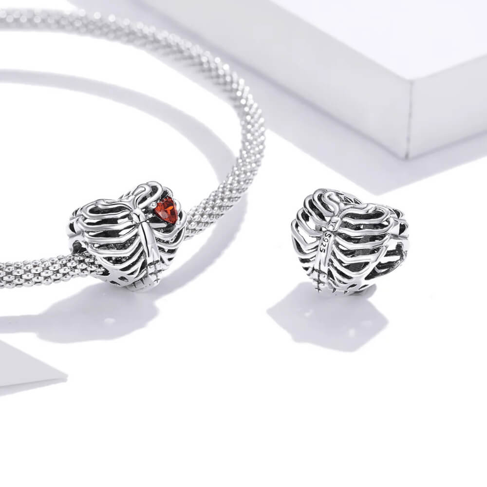 Sterling silver ribcage-shaped charm with an openwork design and a small red heart-shaped crystal inside 
