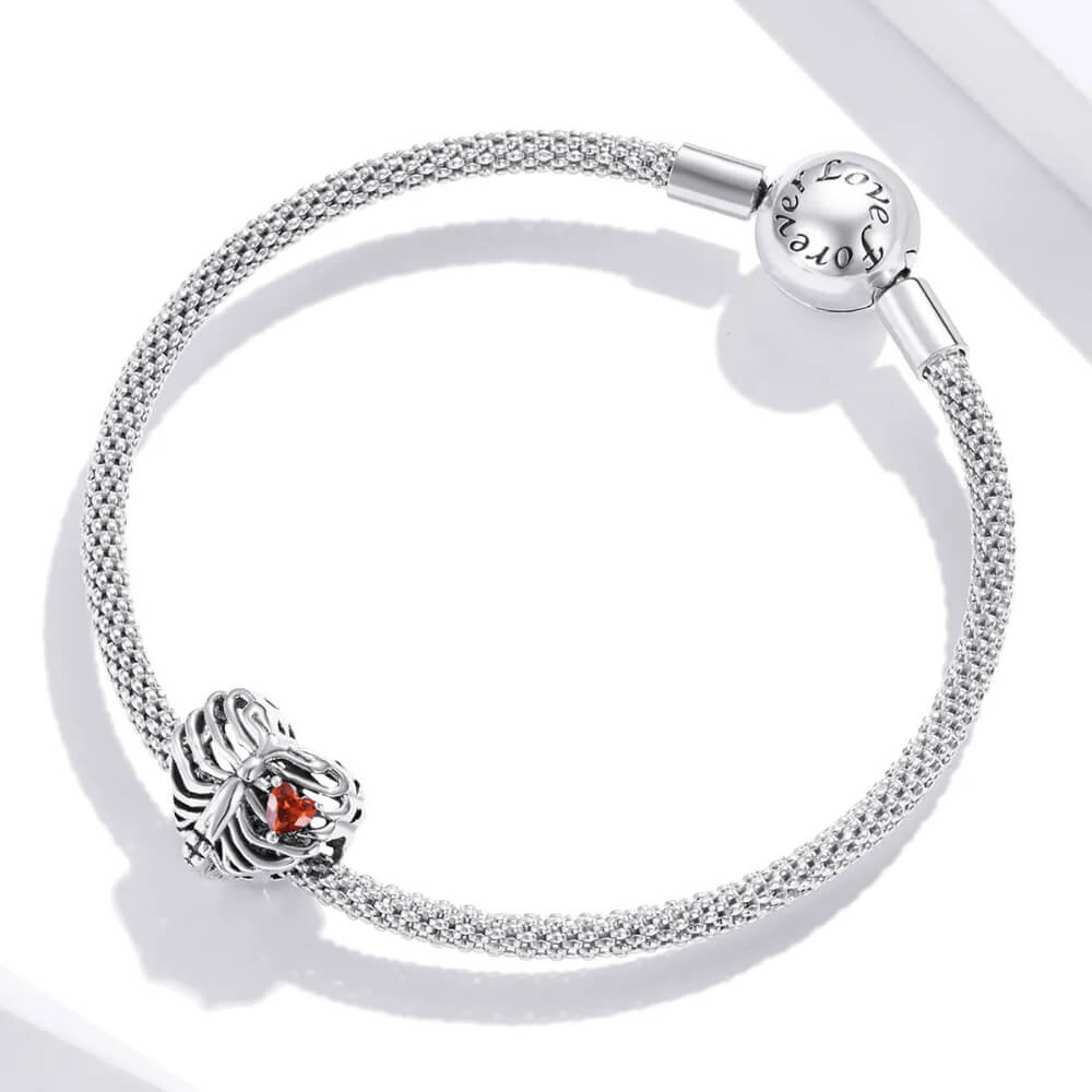 Sterling silver ribcage-shaped charm with an openwork design and a small red heart-shaped crystal inside 