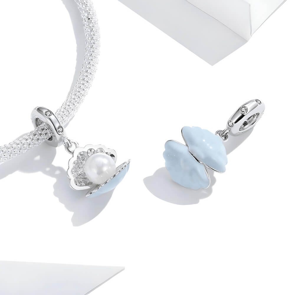 Sterling silver seashell charm with clear gemstones and a dangling white pearl bead.