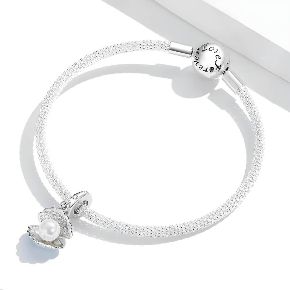 Sterling silver seashell charm with clear gemstones and a dangling white pearl bead.