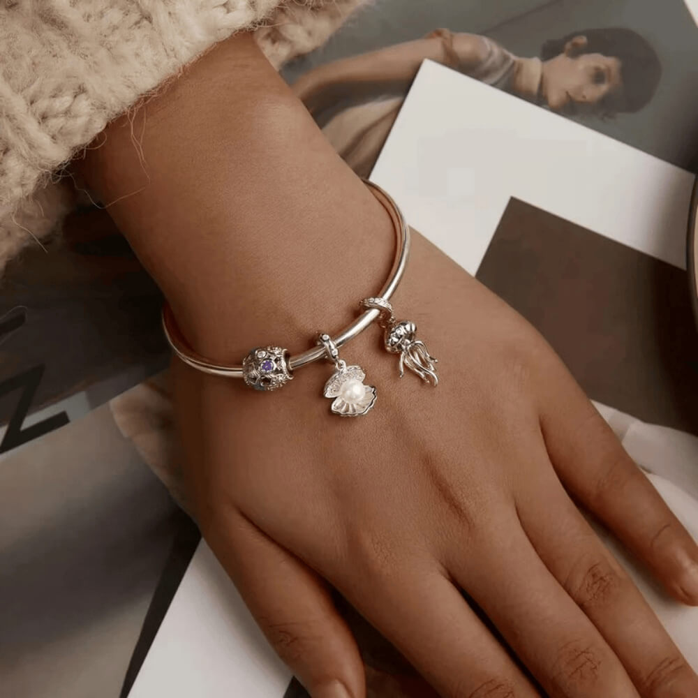Sterling silver seashell charm with clear gemstones and a dangling white pearl bead.