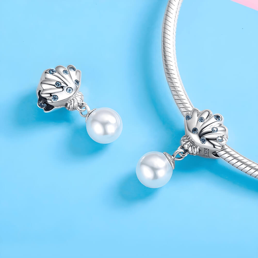 Sterling silver shell charm with blue gemstones and a dangling white pearl.