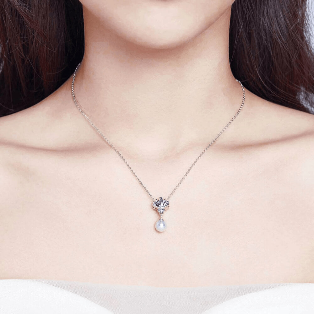 Sterling silver shell charm with blue gemstones and a dangling white pearl.