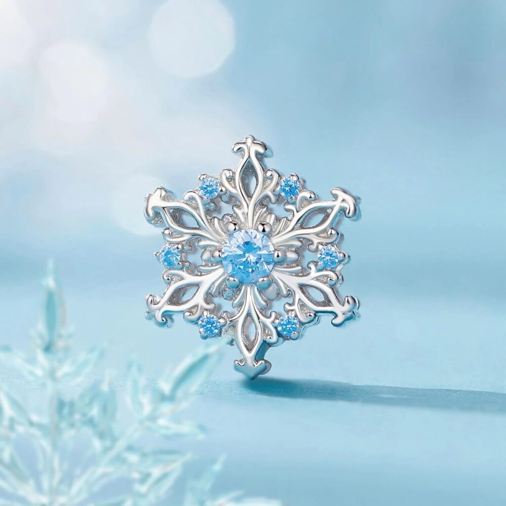 Sterling silver snowflake charm with detailed openwork design and light blue gemstones.