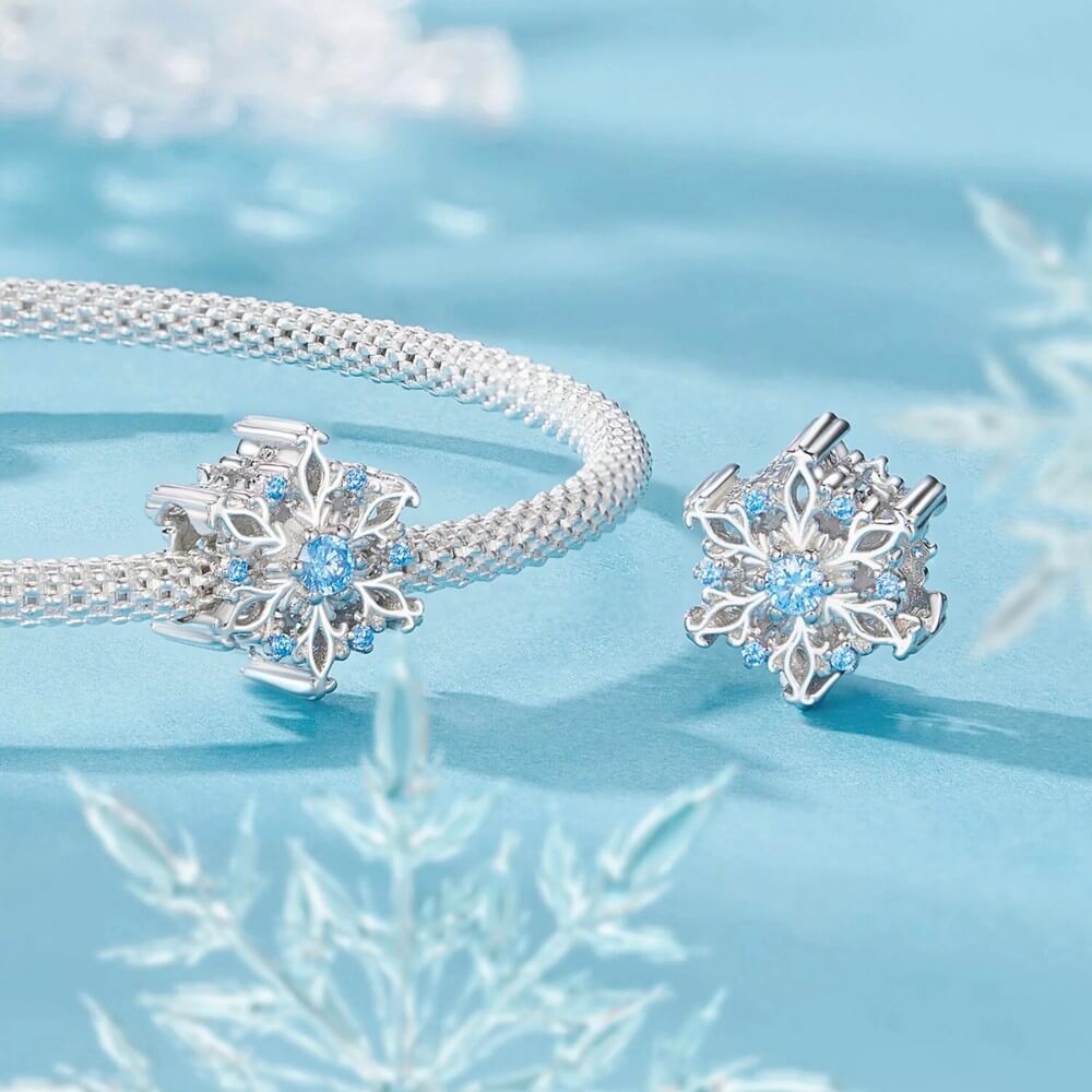 Sterling silver snowflake charm with detailed openwork design and light blue gemstones.