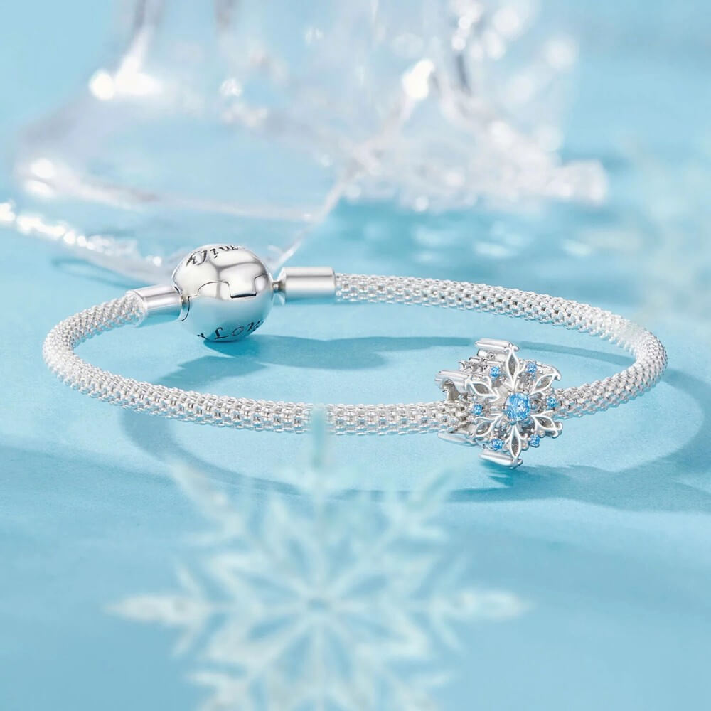 Sterling silver snowflake charm with detailed openwork design and light blue gemstones.