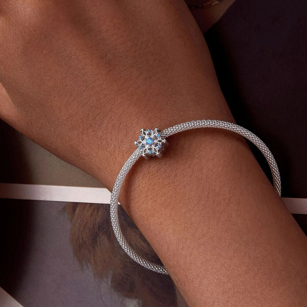 Sterling silver snowflake charm with detailed openwork design and light blue gemstones.