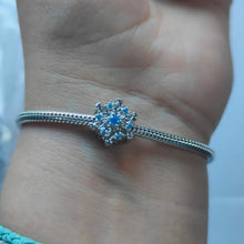 Sterling silver snowflake charm with detailed openwork design and light blue gemstones.
