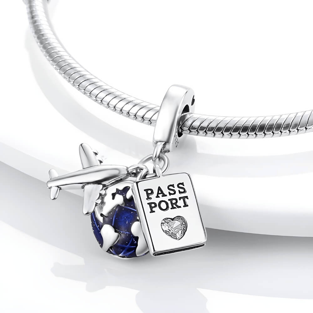 Sterling silver charm with three dangles: a silver airplane, a blue-enamel globe, and a passport tag with a small clear heart-shaped stone 