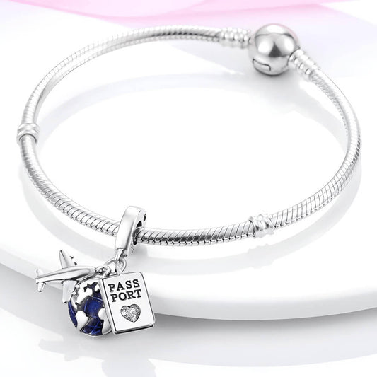 Sterling silver charm with three dangles: a silver airplane, a blue-enamel globe, and a passport tag with a small clear heart-shaped stone 