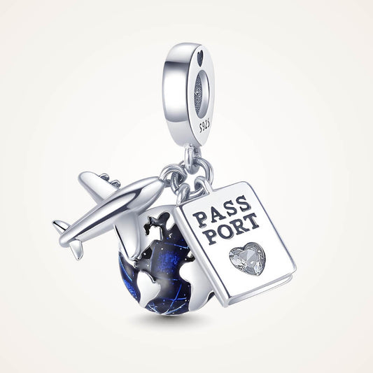 Sterling silver charm with three dangles: a silver airplane, a blue-enamel globe, and a passport tag with a small clear heart-shaped stone – ORÉYA.