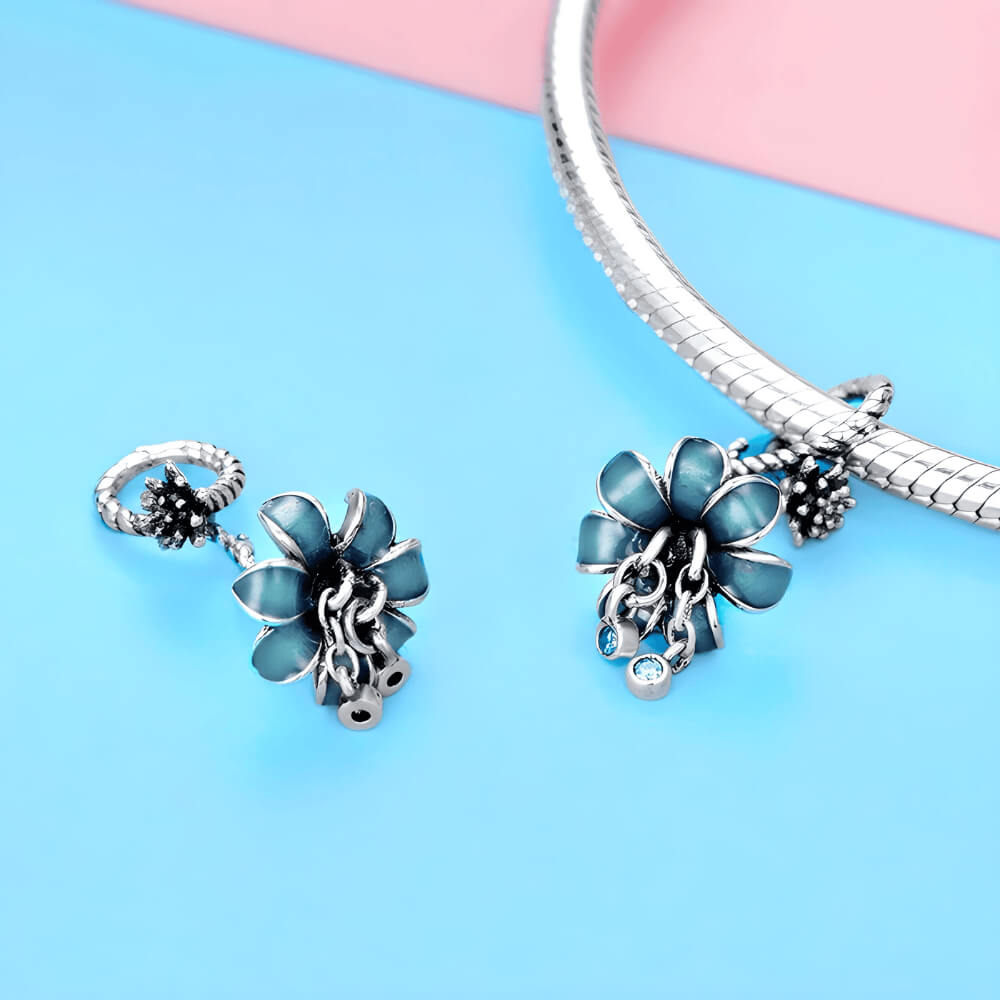 Sterling silver charm with a flower-shaped umbrella design, teal enamel petals, and two dangling blue crystals 