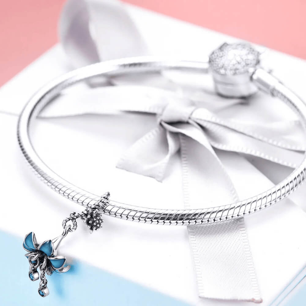 Sterling silver charm with a flower-shaped umbrella design, teal enamel petals, and two dangling blue crystals
