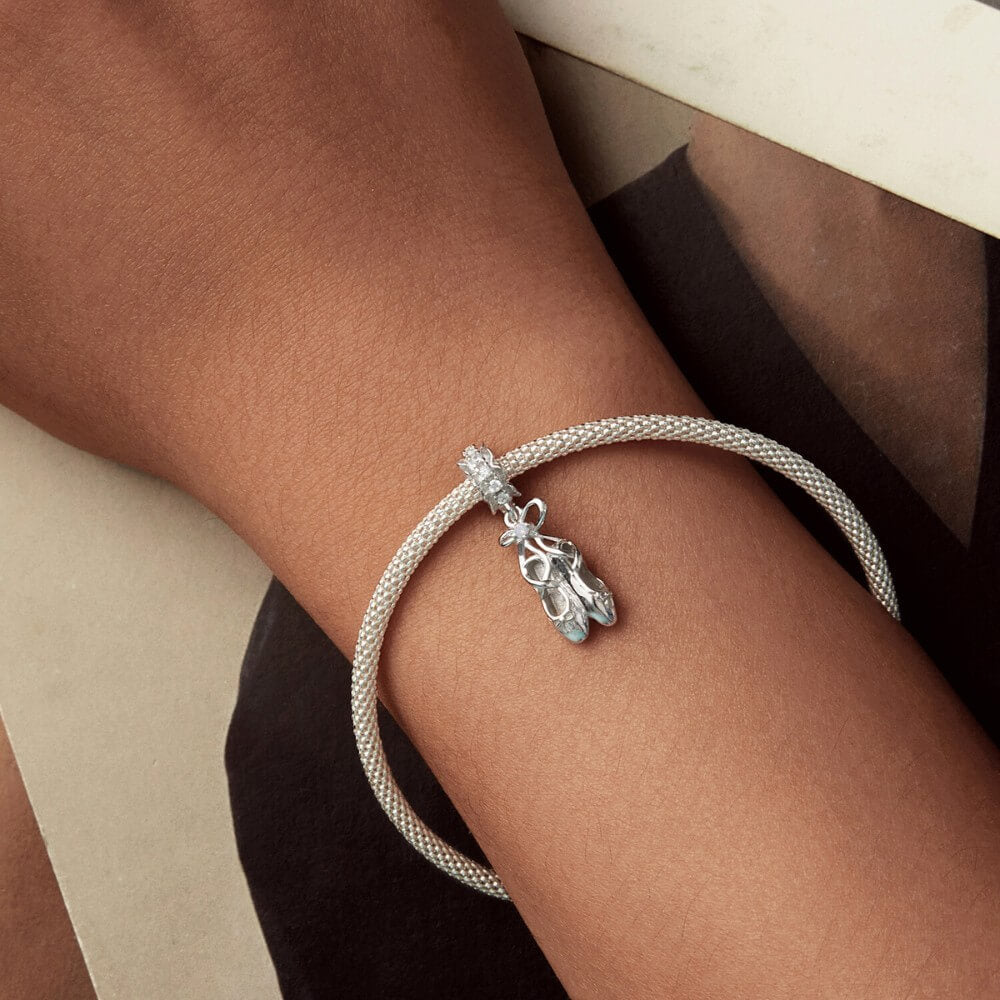 Sterling silver ballet shoes charm with delicate bow and soft pink opalescent detail.