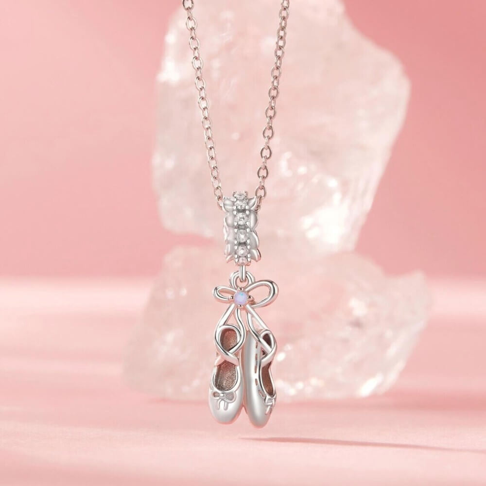 Sterling silver ballet shoes charm with delicate bow and soft pink opalescent detail.