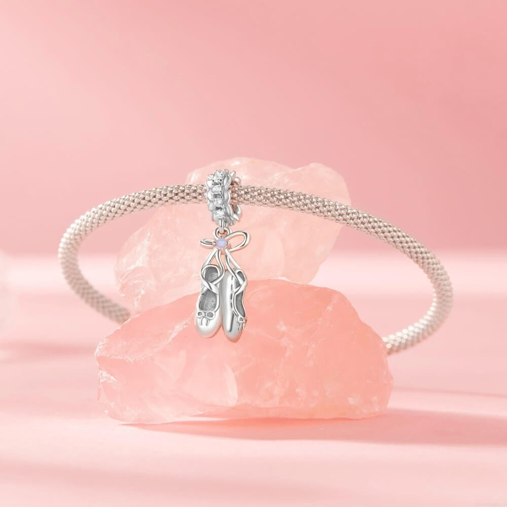 Sterling silver ballet shoes charm with delicate bow and soft pink opalescent detail.