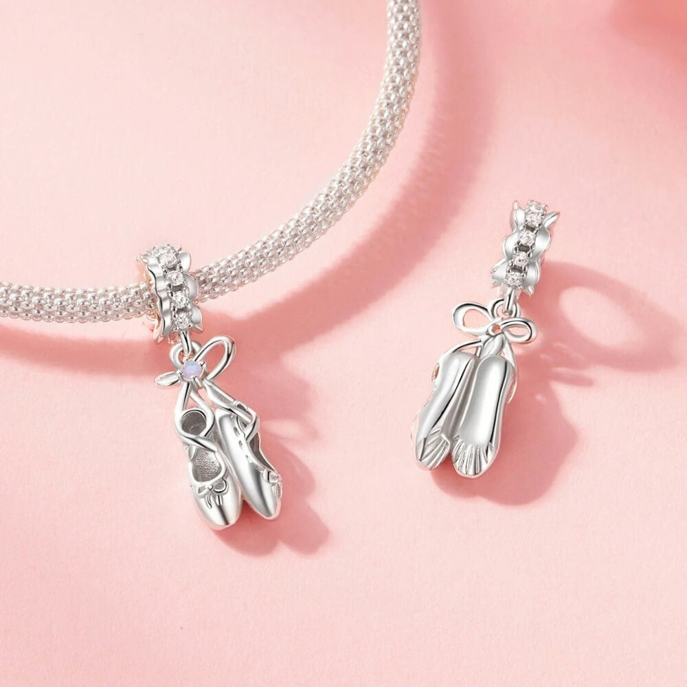 Sterling silver ballet shoes charm with delicate bow and soft pink opalescent detail.