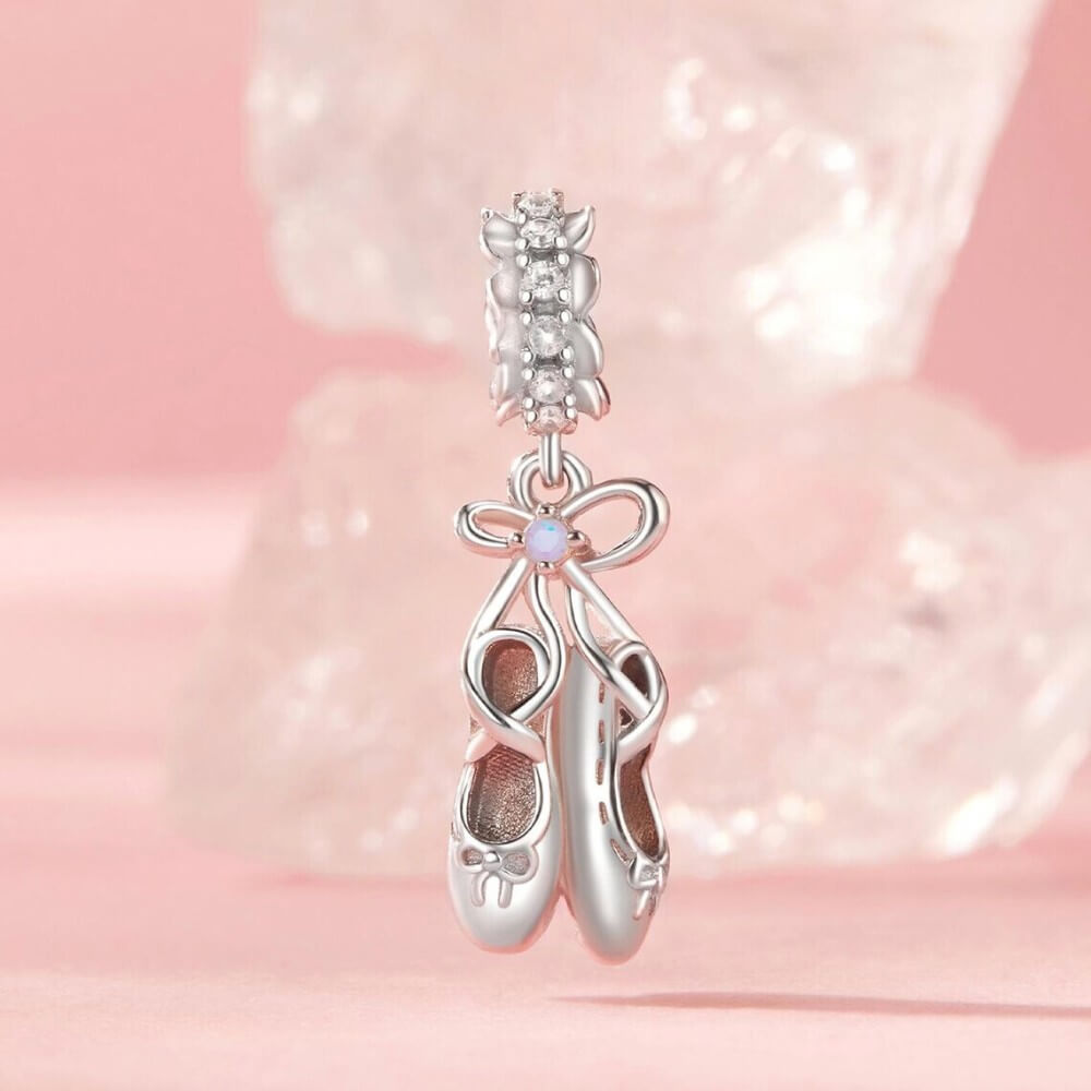 Sterling silver ballet shoes charm with delicate bow and soft pink opalescent detail.