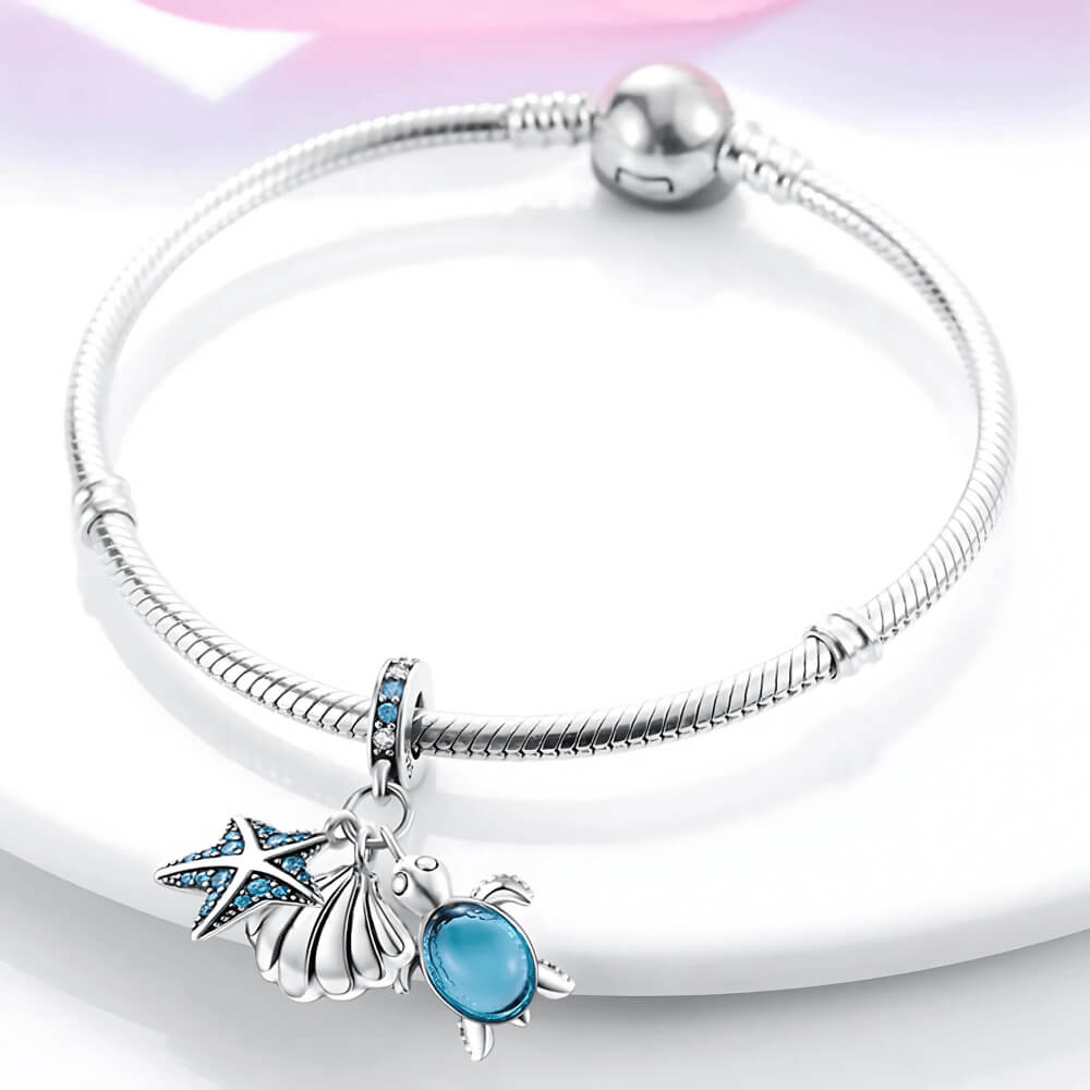 Sterling silver charm with starfish, shell, and blue glass turtle dangles on gemstone bail.