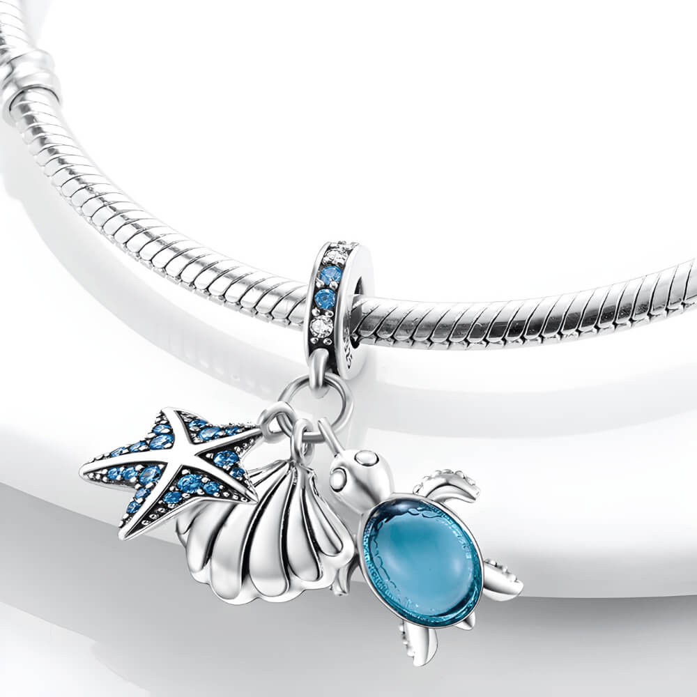 Sterling silver charm with starfish, shell, and blue glass turtle dangles on gemstone bail.