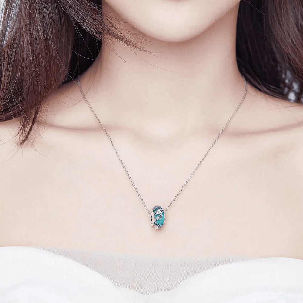Sterling silver mermaid charm wrapped around teal faceted glass bead with textured details.