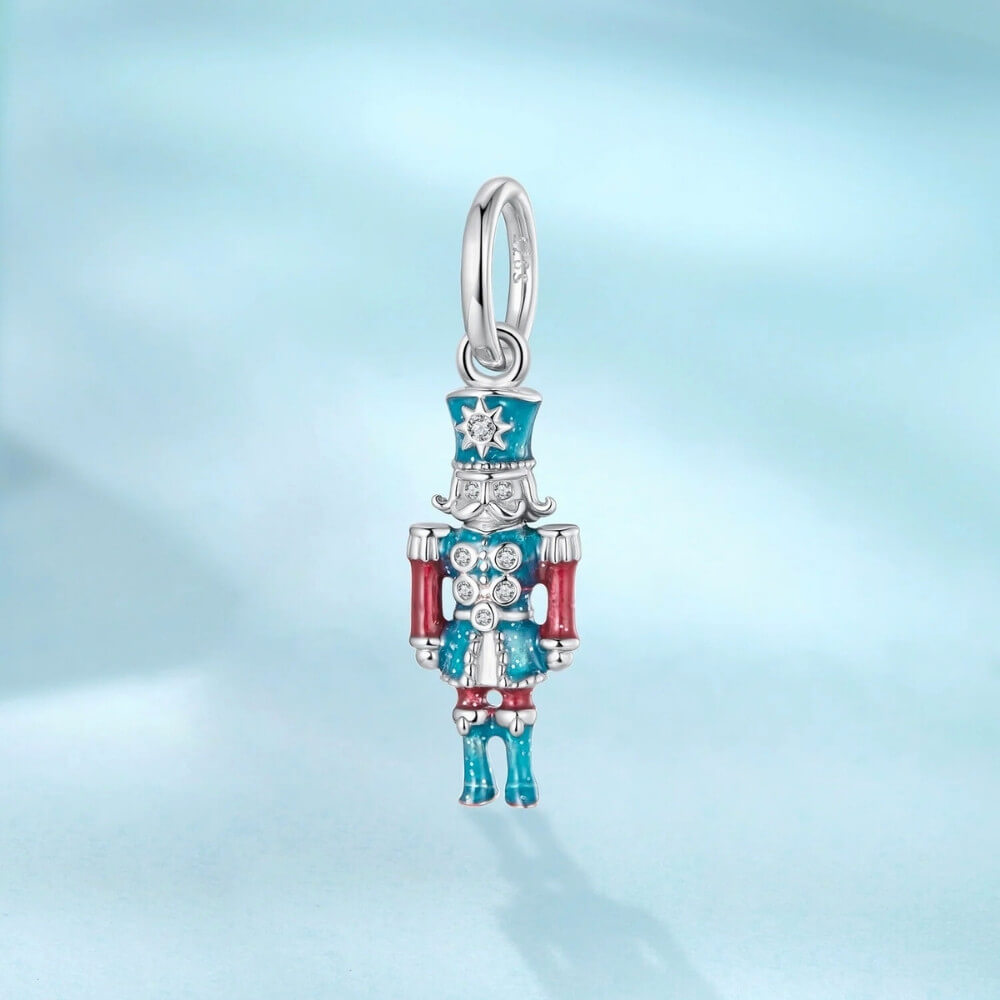 Sterling silver nutcracker charm with teal and red enamel and clear gemstones.