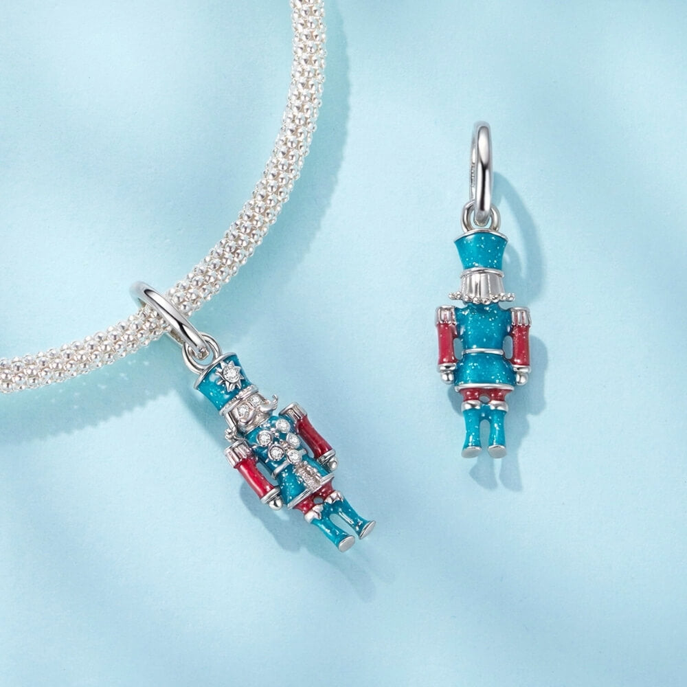 Sterling silver nutcracker charm with teal and red enamel and clear gemstones.