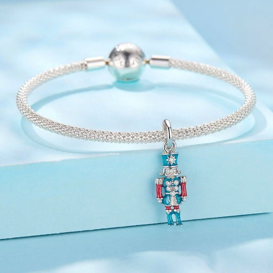 Sterling silver nutcracker charm with teal and red enamel and clear gemstones.