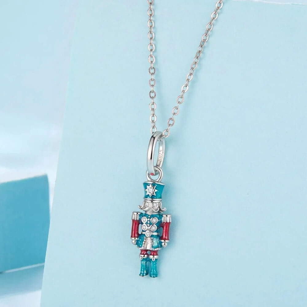 Sterling silver nutcracker charm with teal and red enamel and clear gemstones.