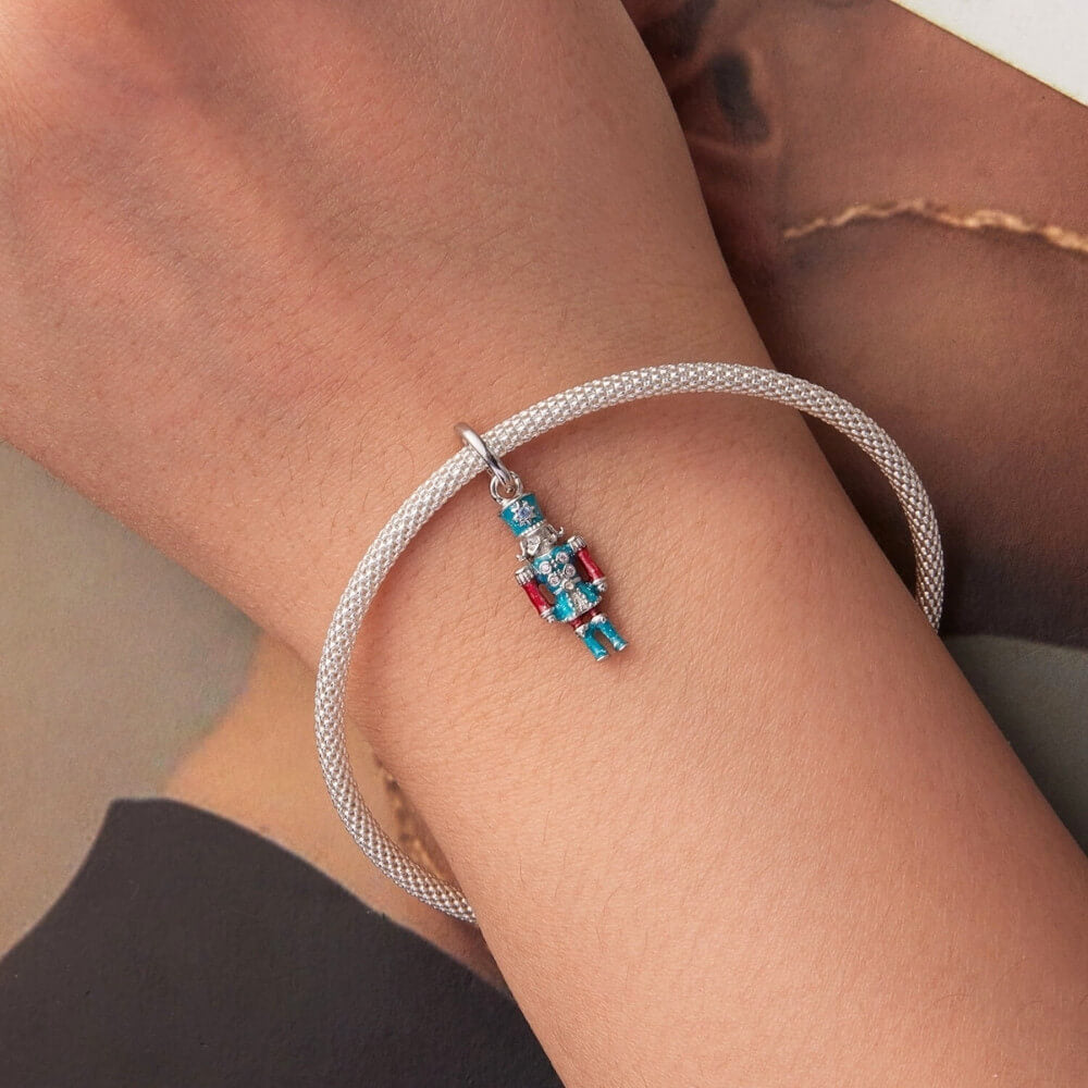 Sterling silver nutcracker charm with teal and red enamel and clear gemstones.