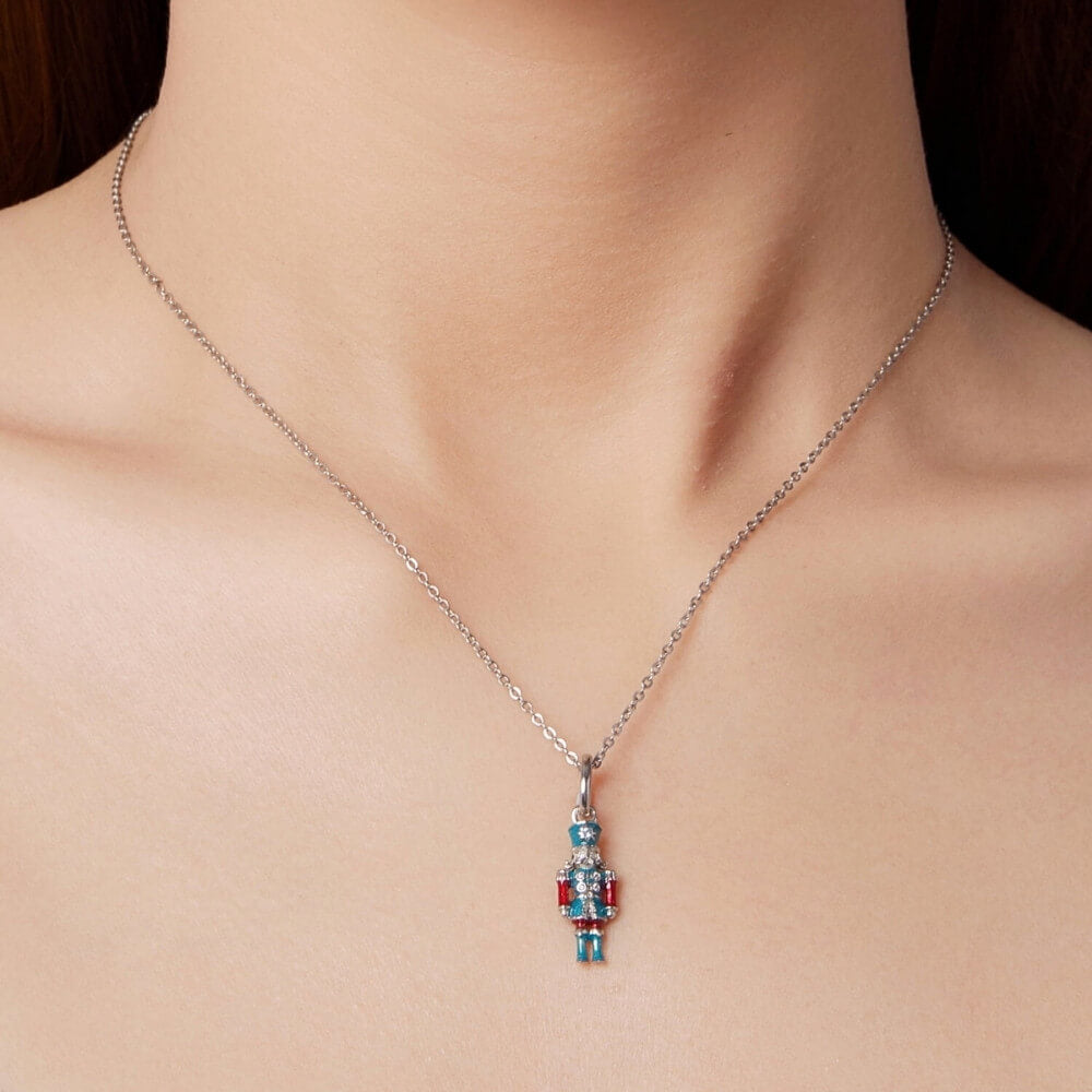 Sterling silver nutcracker charm with teal and red enamel and clear gemstones.