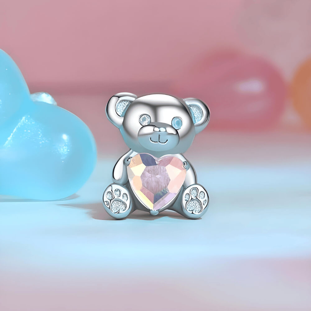Sterling silver teddy bear charm holding an iridescent heart-shaped crystal with paw-print feet 