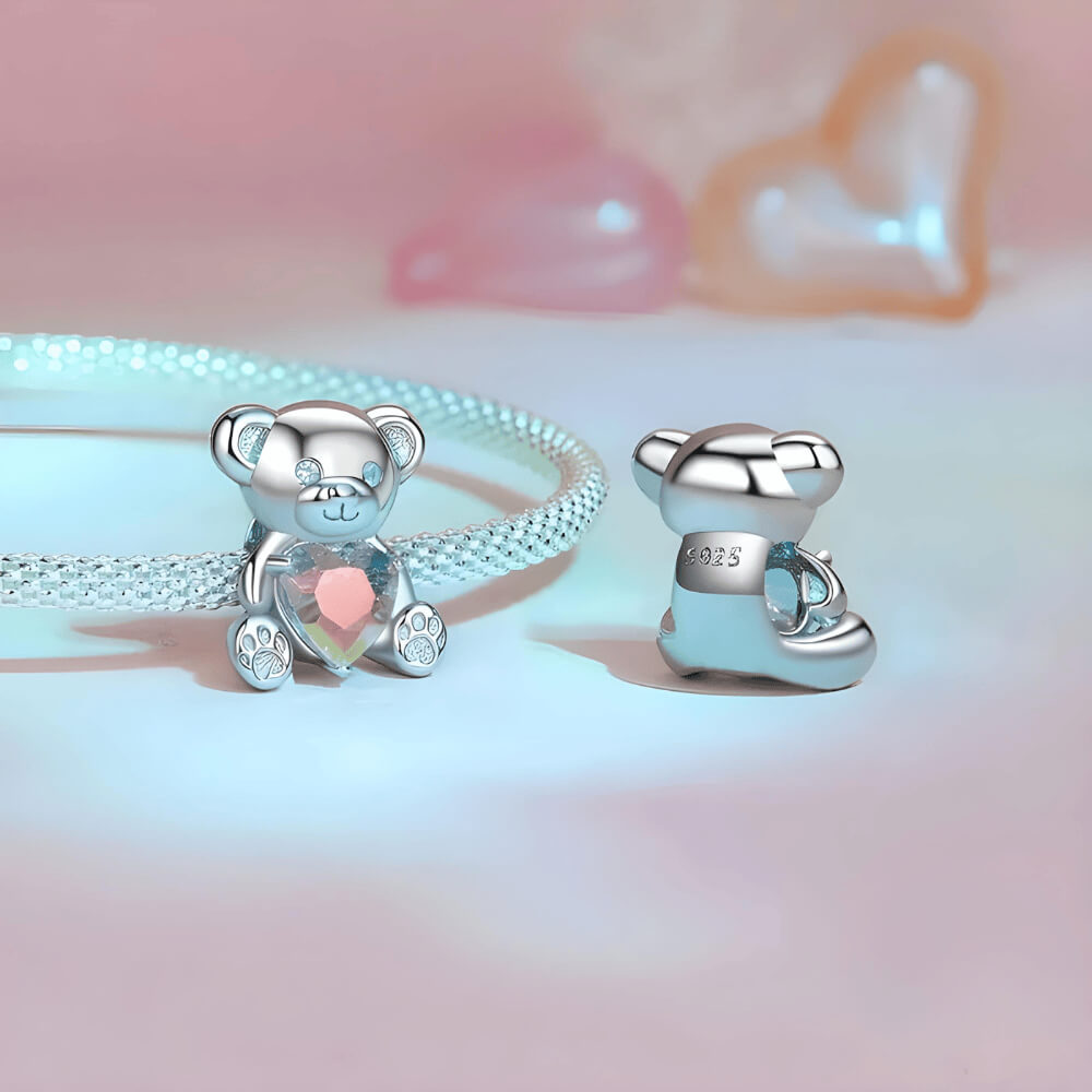 Sterling silver teddy bear charm holding an iridescent heart-shaped crystal with paw-print feet 