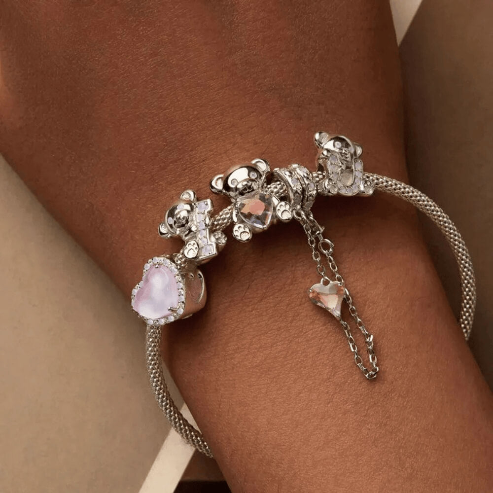 Sterling silver teddy bear charm holding an iridescent heart-shaped crystal with paw-print feet 