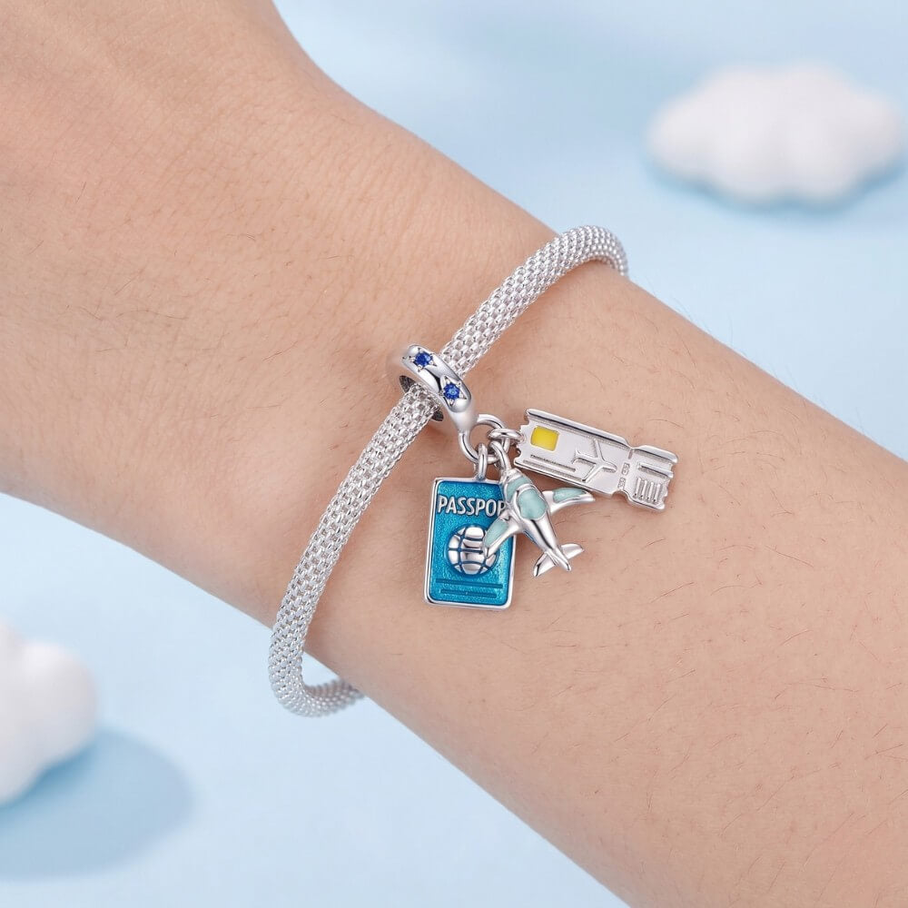 Silver bracelet with travel-themed charms on a wrist against a light blue background