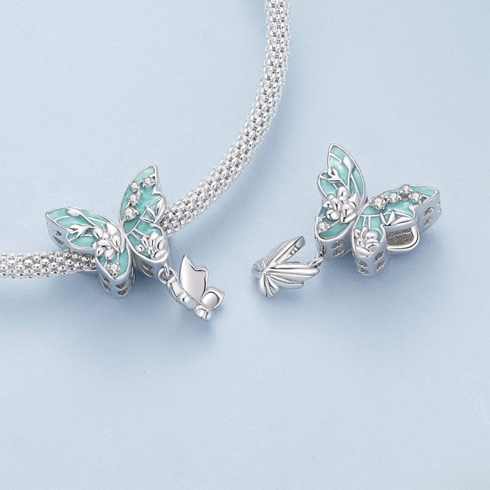 Butterfly-shaped silver and turquoise charm on a chain against a light blue background