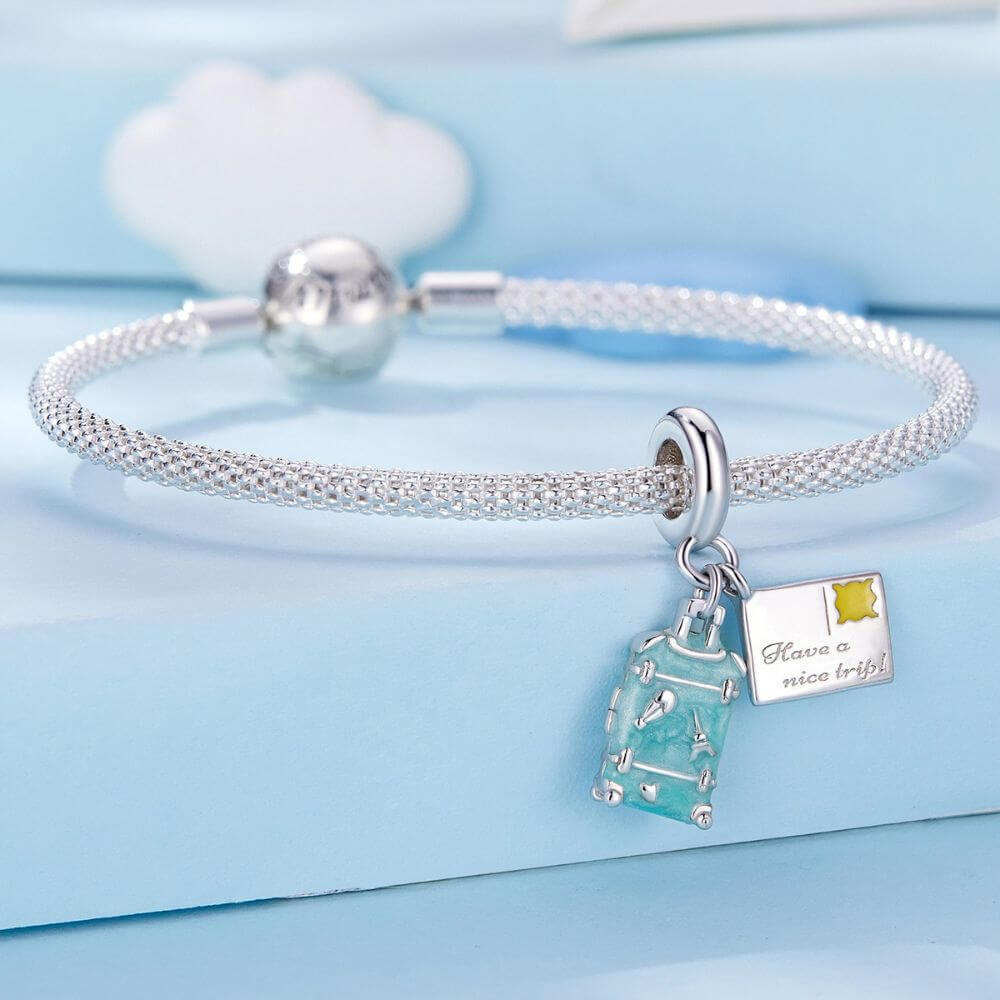 Sterling silver travel charm with turquoise suitcase, postcard, Eiffel Tower, and airplane-inspired details.