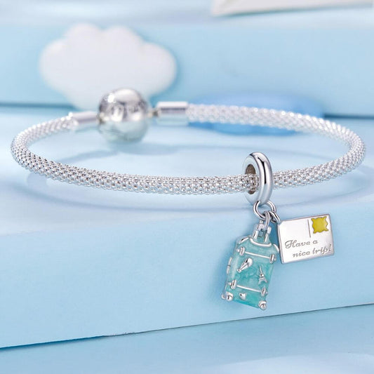 Sterling silver travel charm with turquoise suitcase, postcard, Eiffel Tower, and airplane-inspired details.