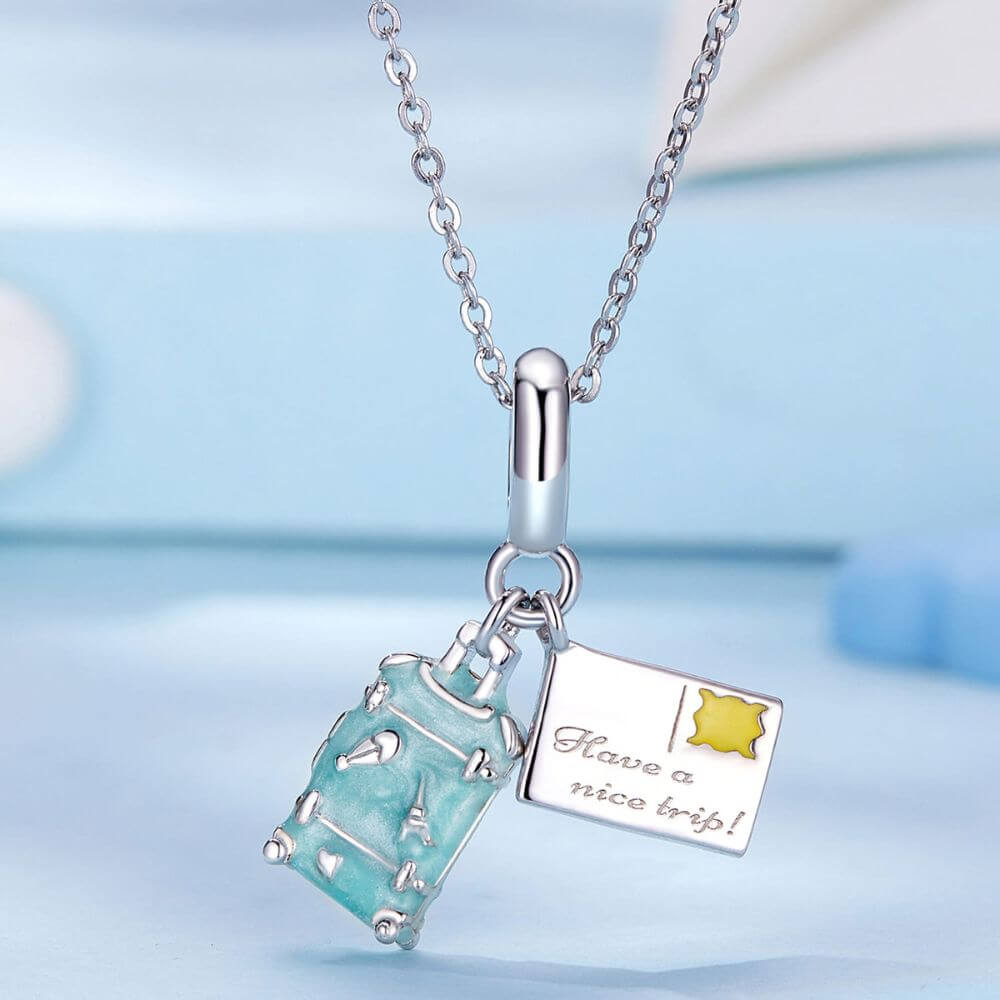 Sterling silver travel charm with turquoise suitcase, postcard, Eiffel Tower, and airplane-inspired details.
