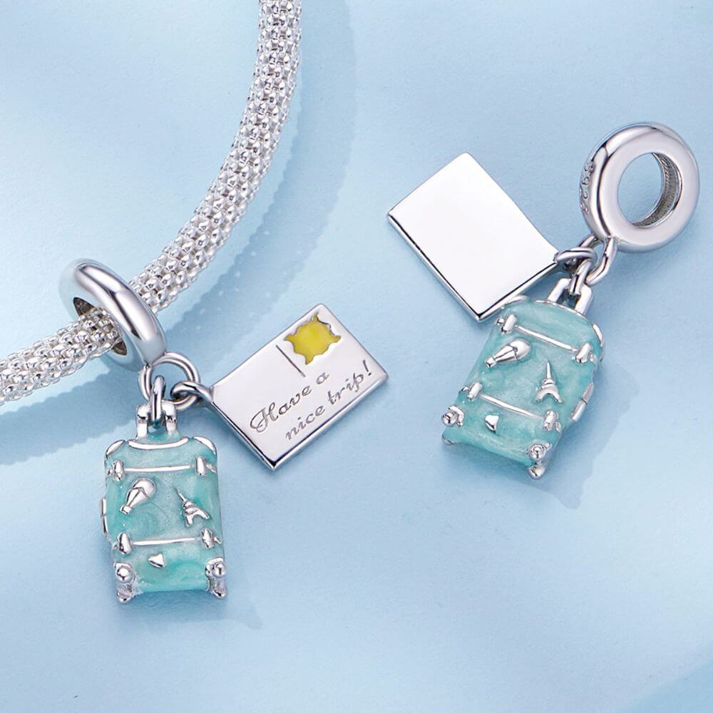 Sterling silver travel charm with turquoise suitcase, postcard, Eiffel Tower, and airplane-inspired details.