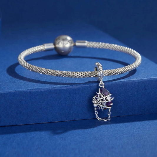 Sterling silver spider charm with violet crystal, web cage, and chain detail.