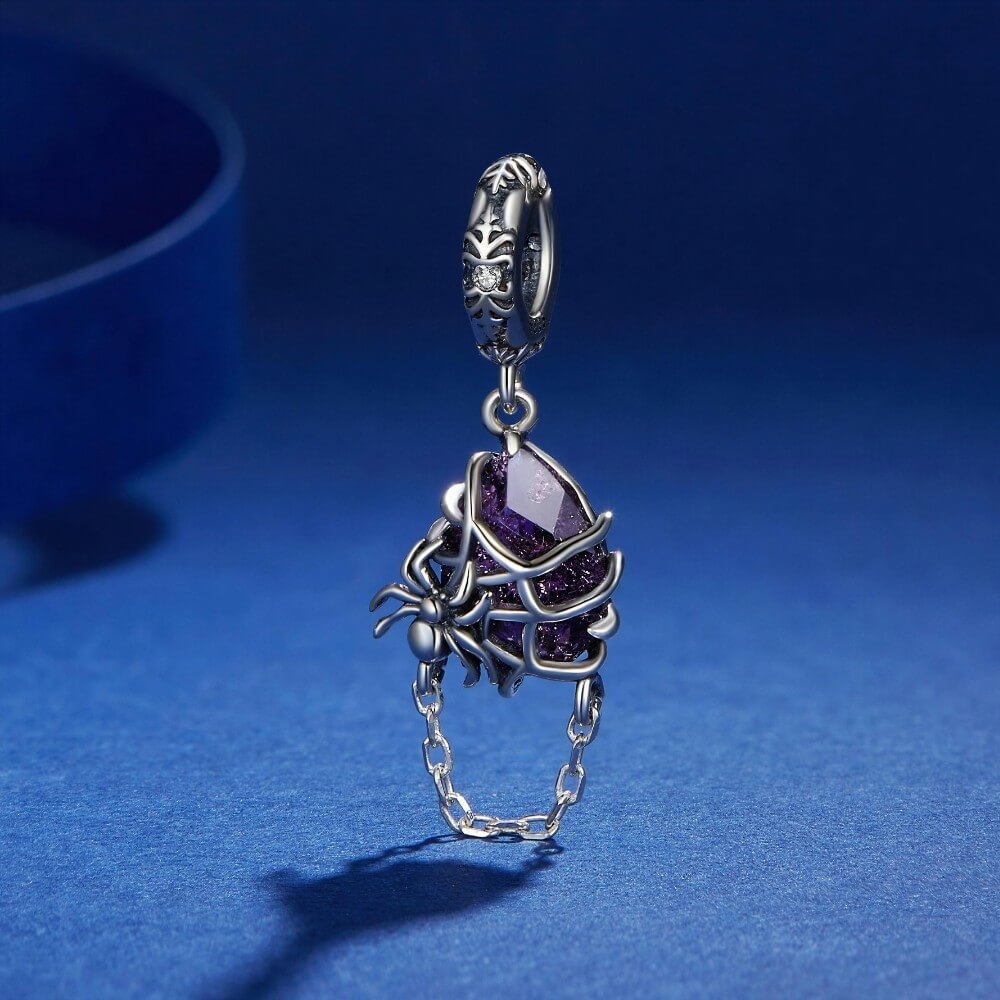 Sterling silver spider charm with violet crystal, web cage, and chain detail.